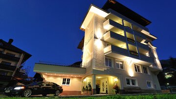 A modern building at night, illuminated with warm light. A black car is parked in the foreground.