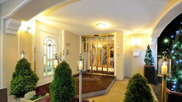 An inviting entrance area with a stylish door section. On both sides, there are green plants and decorative lighting.