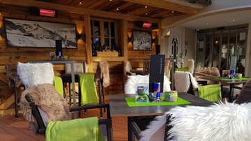 A cozy restaurant with wooden decor and modern furniture. The tables are decorated with colorful tablecloths and decorations.