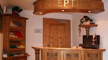 A cozy hotel reception made of wood with a reception desk. In the background, there is a shelf with informational materials.