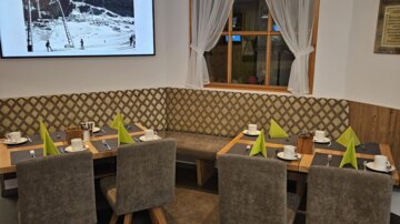 A modern restaurant with cozy seating and tables. A screen is mounted on the wall, displaying an image.