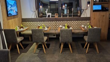 A modern restaurant with wooden furniture and a cozy atmosphere. There are several tables with chairs and a large window front.