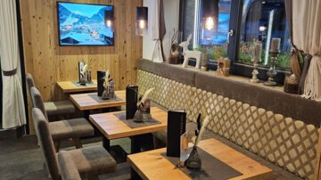 A cozy restaurant with wooden tables and upholstered benches. A television hangs on the wall, and the atmosphere is warm and inviting.