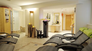 A relaxing wellness area with loungers, soft lighting, and a modern design. In the background, a shower and a reception desk are visible.