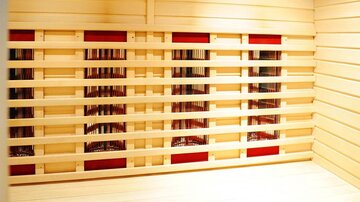 A bright sauna room with wood paneling and electrically operated infrared heaters. The walls are simple and invite relaxation.