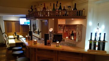 A cozy bar with a wooden counter and a selection of drinks. In the background, seating and a television are visible.