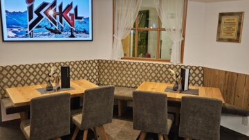 A cozy restaurant area with wooden tables and upholstered chairs. In the background, a television with the inscription "Ischgl" is visible.
