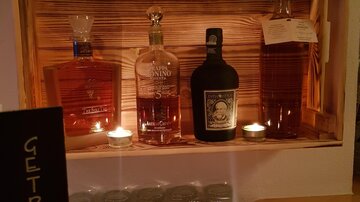 A selection of spirits in a wooden box, illuminated by tealights. In the foreground, there is a sign reading "DRINKS".
