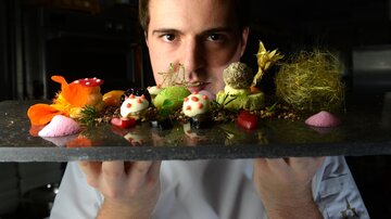 A chef presents artfully arranged desserts on a serving platter. The treats are colorful and decoratively designed.