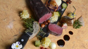 A stylishly served dish with tender meat, various sides, and decorative ingredients. The presentation shows creativity and culinary artistry.