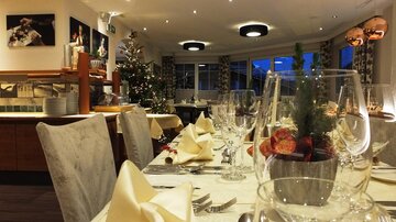 An elegant restaurant with festively set tables and a Christmas tree. The atmosphere is warm and inviting, perfect for special occasions.