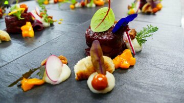 An artistically arranged plate with tender meat, colorful vegetable sides, and edible flowers. The presentation is modern and appealingly designed.