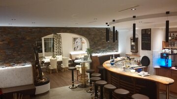 A modern restaurant with a stylish bar and comfortable seating areas. The decor combines wood and stone for an elegant ambiance.