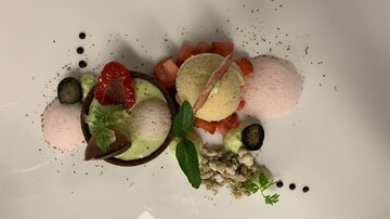 An artfully arranged dessert with various scoops of ice cream, fresh strawberries, and mint. The presentation is colorful and appealing on a white plate.