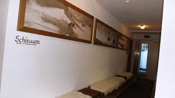 A narrow hallway with wooden frames and pictures of winter sports. On the left side, there is a bench with sheepskins.