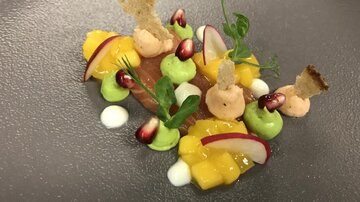 An artfully arranged dish with fresh ingredients. It contains colorful elements such as mango, radishes, and various sauces.