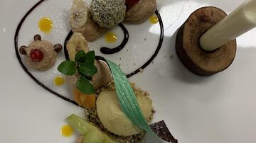 An artistically presented dessert with various textures and colors. It includes fruit, ice cream, and decorative sauces.