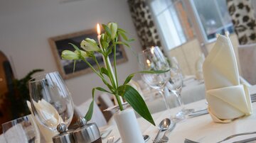 An elegantly set table with glasses, cutlery, and a flower vase. The candle creates a cozy atmosphere.