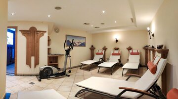 A relaxing wellness area with loungers and a fitness machine. The room is well lit and inviting.
