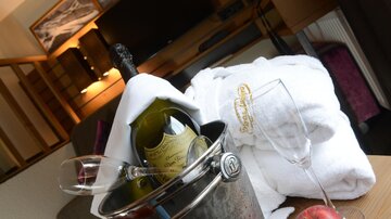 An elegant suite with a cool bottle of champagne in an ice bucket. Next to the champagne, there is a glass and a red apple on the table.