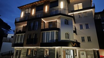 A modern building with multiple balconies and appealing lighting at night. The facade combines different materials and features clear lines.