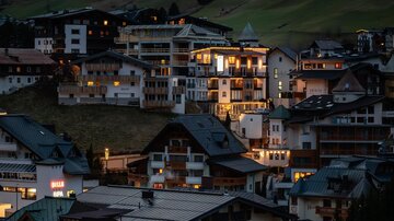 A picturesque mountain town at night, illuminated by warm lights. The buildings are surrounded by a serene, natural environment.