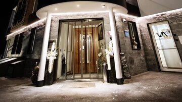 A modern hotel building at night, illuminated with warm light. The facade is elegantly designed and showcases the entrance area with glass and decoration.