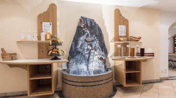 A stylishly designed wellness area with a water feature and wooden shelves. Fruits and various drinks are displayed on the shelves.