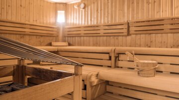 A cozy wooden sauna with benches and a bucket. Soft light filters through a window, creating a relaxing atmosphere.