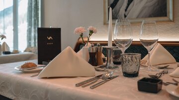 An elegantly set table with two wine glasses, cutlery, and decorative napkins. In the background, there is a menu and a small flower vase.