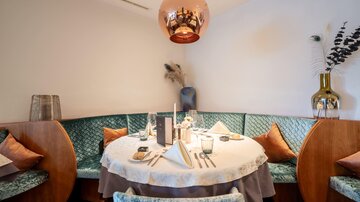An elegant restaurant interior with a round table that is lovingly set. The walls are painted in soft colors, and a stylish lamp hangs from the ceiling.