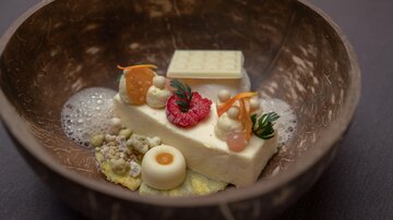 An artistic dessert in a bowl with various textures and colors. It features an ice cream-like base, fresh fruits, and decorative elements.