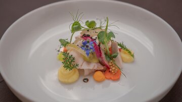 A beautifully arranged plate with tender fish, fresh vegetables, and colorful sauces. The decoration of edible flowers and herbs gives the dish an elegant touch.
