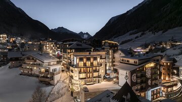 A charming mountain village with snow-covered houses and illuminated windows. The surrounding landscape is shaped by majestic mountains.
