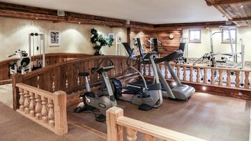 Ein moderner Fitnessraum mit verschiedenen Geräten. Die Wände sind mit Holz ausgekleidet und es gibt große Fenster für natürliches Licht.
