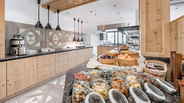 Eine moderne Küche mit Holzverkleidungen und eleganten Pendelleuchten. Auf dem Tisch sind verschiedene Gläser mit Snacks und Backwaren angerichtet.