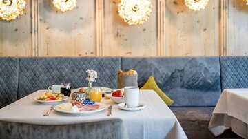 Ein elegantes Frühstückstisch mit verschiedenen Speisen, darunter Obst und Gebäck. Die Wand ist mit stilvollen Lichtquellen dekoriert, die eine gemütliche Atmosphäre schaffen.