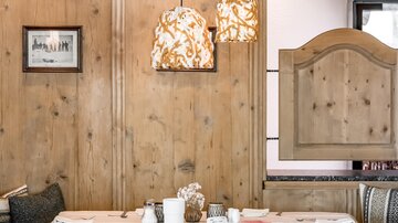Ein stilvolles Restaurant mit holzverkleideten Wänden und modernen Pendelleuchten. Der Tisch ist elegant gedeckt und schafft eine einladende Atmosphäre.