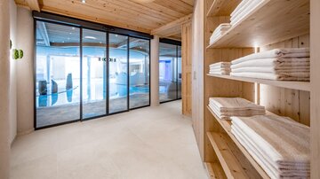 Ein moderner Wellnessbereich mit holzverkleideten Wänden und einem klaren Blick auf einen Pool. Regal mit gefalteten Handtüchern sorgt für eine entspannende Atmosphäre.