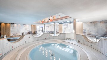Ein eleganter Wellnessbereich mit einem runden Whirlpool. Helle Farben und moderne Ausstattung schaffen eine entspannende Atmosphäre.