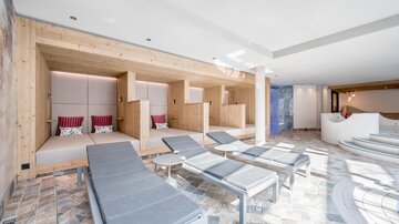 Ein moderner Wellnessbereich mit gemütlichen Liegen und Holzdetails. Tageslicht strömt durch große Fenster und schafft eine entspannende Atmosphäre.