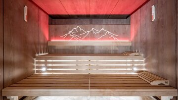 Eine moderne Sauna mit Holzbank und sanftem Licht. Die Wand zeigt eine stilisierte Berglandschaft.