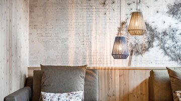 Eine stilvolle Lounge mit gemütlichen Sofas und modernen Lampen. Die Wände sind aus hellem Holz und Ziegelstein, was eine einladende Atmosphäre schafft.