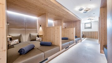 Ein entspannender Ruheraum mit Holzverkleidung und gemütlichen Liegen. Jeder Bereich ist durch Wände abgetrennt und schafft eine ruhige Atmosphäre.
