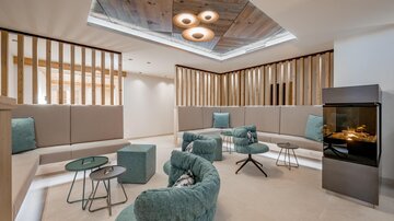 Ein moderner Lounge-Bereich mit gemütlichen Sitzgelegenheiten und warmem Licht. Die Wände bestehen aus Holz und die Atmosphäre ist einladend und entspannt.