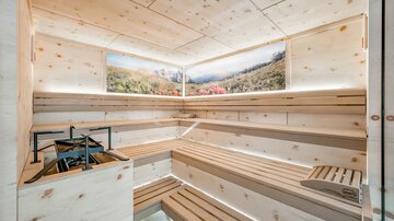 Eine moderne Sauna mit Holzbänken und sanften Beleuchtungen. An den Wänden sind Landschaftsbilder zu sehen, die eine entspannende Atmosphäre schaffen.