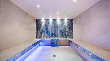 Ein modernes Spa mit elegantem Design und sanfter Beleuchtung. Die Wände sind mit edel verarbeitetem Material verkleidet, was eine entspannende Atmosphäre schafft.