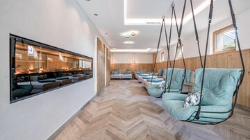 Ein stilvoller Raum mit hängenden Sesseln und einem modernen Kamin. Die Holzverkleidung und sanfte Farben schaffen eine entspannende Atmosphäre.