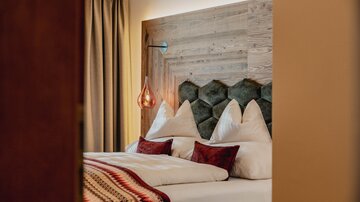 Ein stilvolles Schlafzimmer mit einem gemütlichen Doppelbett und einem modernen Kopfteil aus Holz. Die warmen Farben und die dekorativen Kissen schaffen eine einladende Atmosphäre.