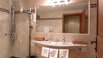Ein modernes Badezimmer mit einer großen, eleganten Dusche und einem Doppelwaschbecken. Der Spiegel reflektiert die stilvolle Einrichtung und die hellen Wände.